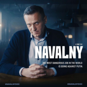 A deep blue-toned photo of Alexey Navalny, a clean-cut middle aged white Russian man in an open collared white shirt and dark blue blazer, He sits at a table with a glass of water, his hands crossed before him, chin tilted down, look up intensely at the viewer. Text on the image says: "Winner: Best political Documentary. Critics Choice Awards. A CNN Film. Navalny. The Most Dangerous Job in the World is Going Against Putin. HBO Max: Now Playing."