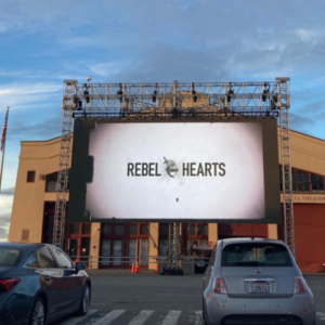 Image of an outdoor movie theater. On the movie screen are the words Rebel Hearts 