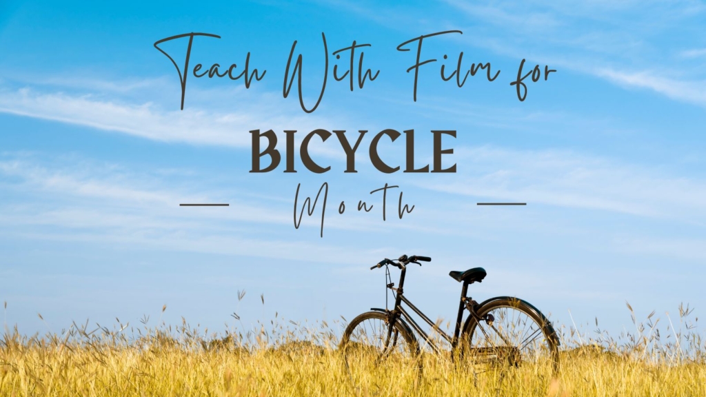 A simple black bicycle stands in a field of tall, dry grasses under a blue sky. Text across the top says "Teach with Film for Bicycle Month.
