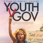 Detail from the film poster for Youth v Gov, showing a boy of color at a climate protest, his fist upraised. A protest sign over his shoulder says: "See You in Court."