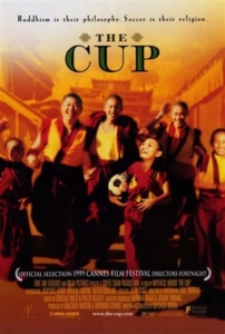 The film poster for The Cup, showing a group of Tibetan Buddhist monks in saffron robes running forward joyfully in front of a Tibetan Buddhist monastery. A boy monk in front carries a soccer ball. Text at the top above the title says: "Buddhism is their philosophy. Soccer is their religion."