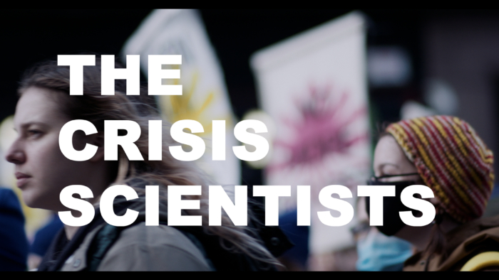 Photograph, in profile, of people at a climate march, signs in the air. Text across the image reads: The Crisis Scientists