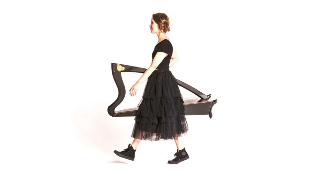 Maeve Gilchrist is shown in profile, facing left. She strides confidently forward in a black dress and black running shoes, with her Celtic harp under her arm. It's a fun, dynamic, engaging portrait. She is featured in the Silk Road American Railroad Project and the series My Music with Rhiannon Giddens.